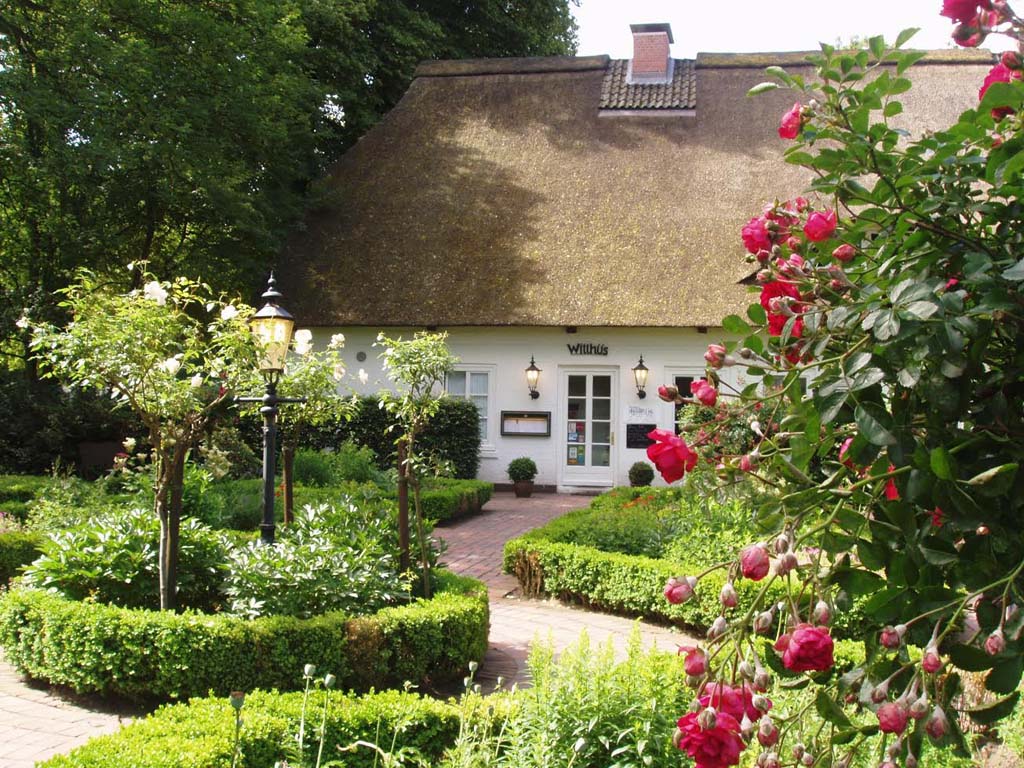 Ein weißes mit Reet gedecktes Haus steht in einem Garten mit Blumen und Bäumen.