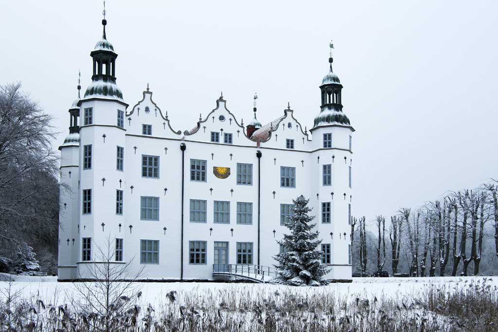 Um das weiße Schloss mit Türmchen in Ahrensburg liegt Schnee.
