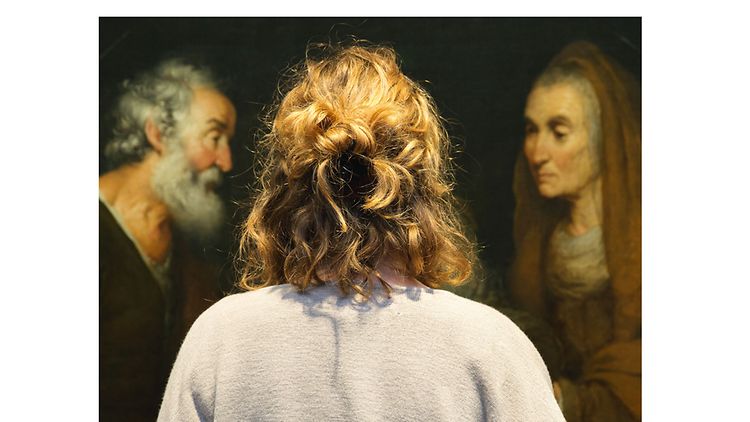  Rückansicht einer lockigen Besucherin vor einem Gemälde 