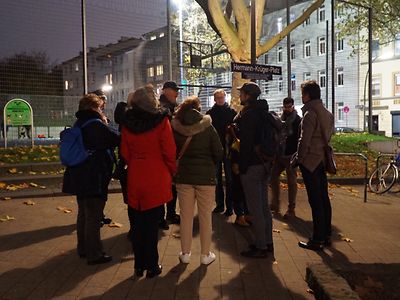  Mehrere Menschen in Winterjacke, die im Dunkeln auf dem Hermann-Krüger-Platz in Harburg versammelt stehen.