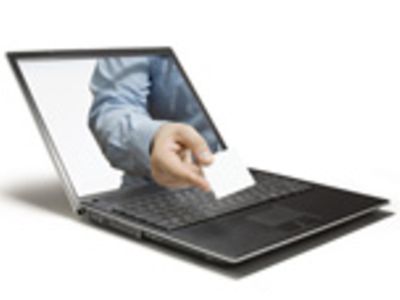 Laptop aus der eine Hand mit Visitenkarte gestreckt wird