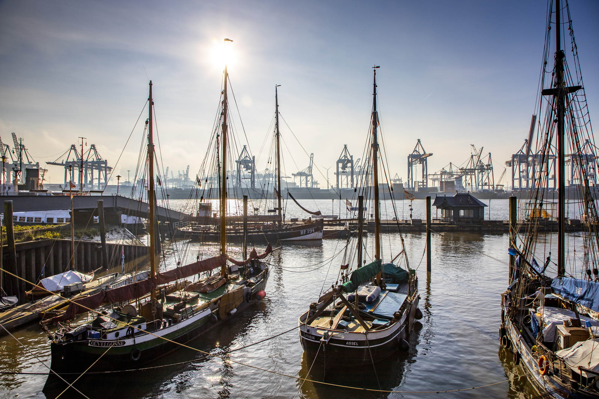 Alte Schiffe liegen im Wasser, im Hintergrund moderne Hafenkrane