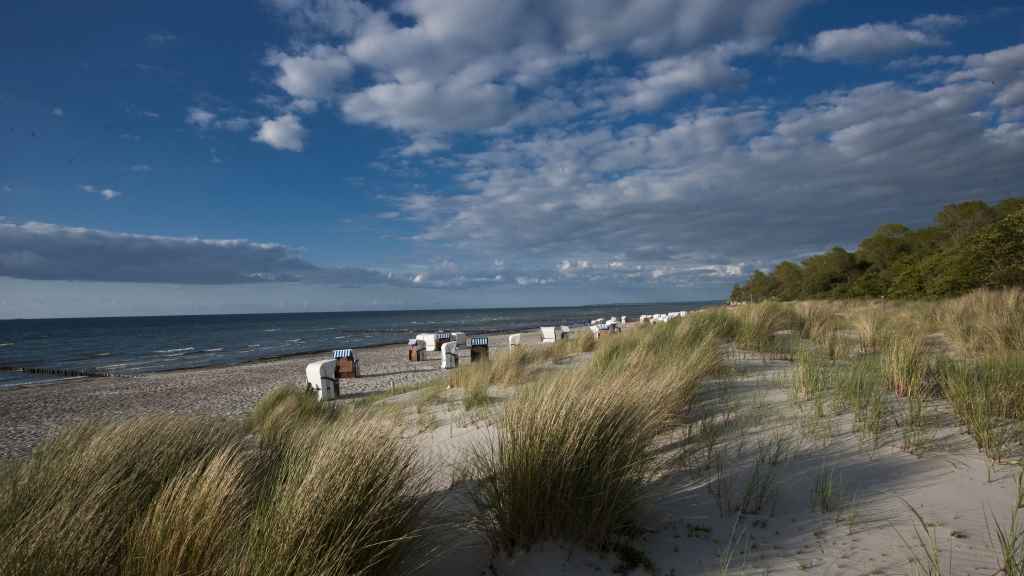 Ein weißer Ostseestrand mit Gras in den Dünen und ein paar Strandkörben.