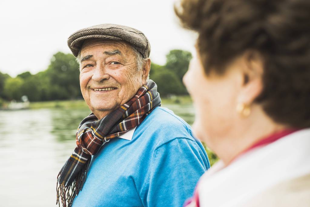 Senioren stehen in der Natur und lächeln sich zu.