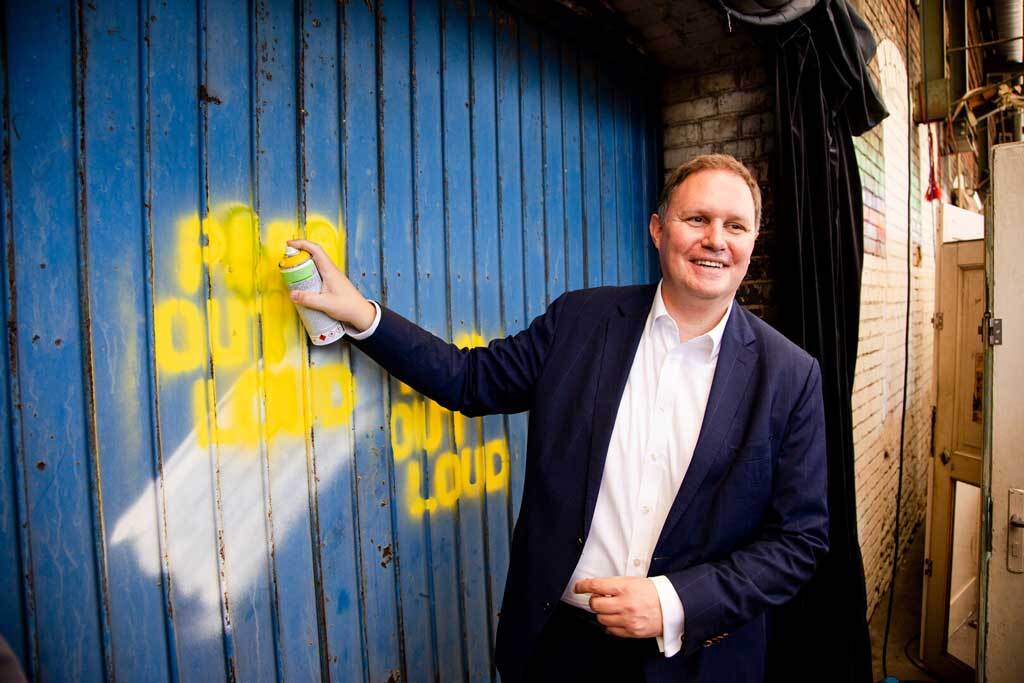 Kultursenator Carsten Brosda sprüht das Motto des Kultursommers Hamburg "Play out loud" an eine Wand