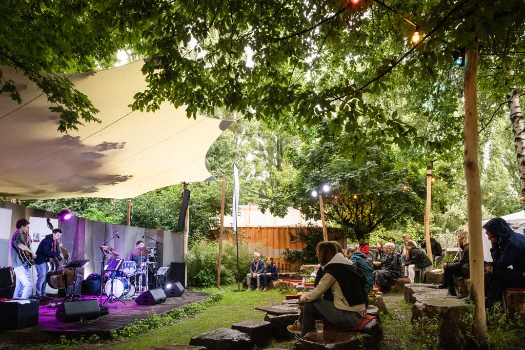 Links im Bild ist die NDR-Bühne beim Kampnagel Sommerfestival zu sehen. Rechts im Bild die ZuschauerInnen im Avant-Garten auf Kampnagel.