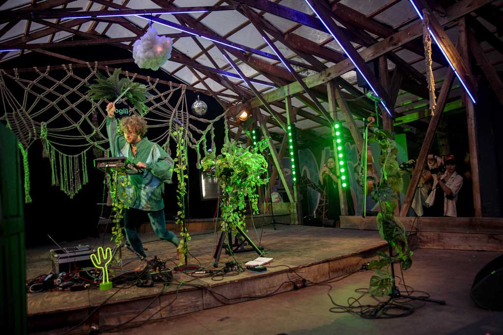 Der Kölner Künstler Moglii bei seinem Auftritt beim Fast ein MS Dockville. Die Bühne ist grün beleuchtet und mit Pflanzen geschmückt.