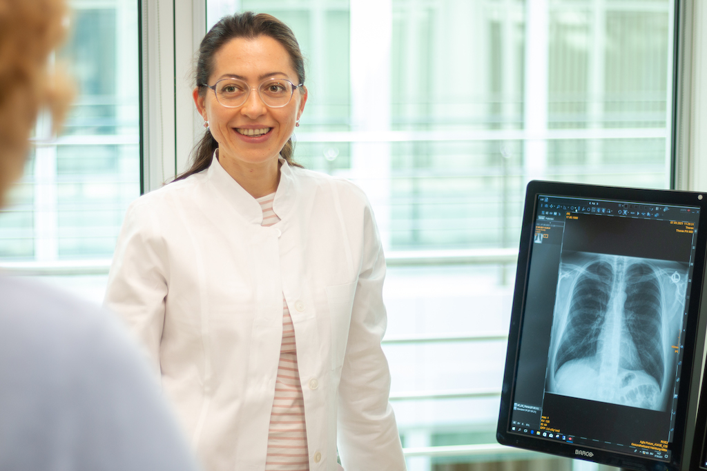 Eine Ärztin steht neben einem Röntgenbild einer Lunge.