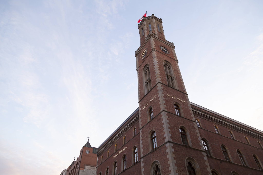 Dunkelrotes Backsteingebäude mit Turm und Hamburg-Fahne auf der Spitze.