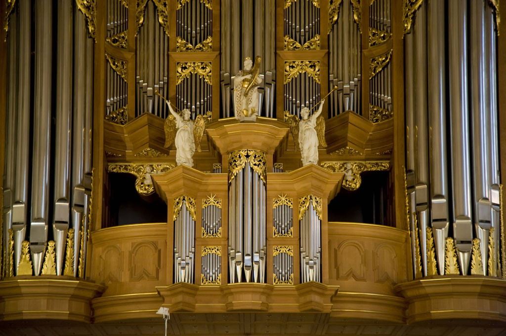 Mit Gold verzierte Orgel mit goldenen Ornamenten und drei weißen Figuren.