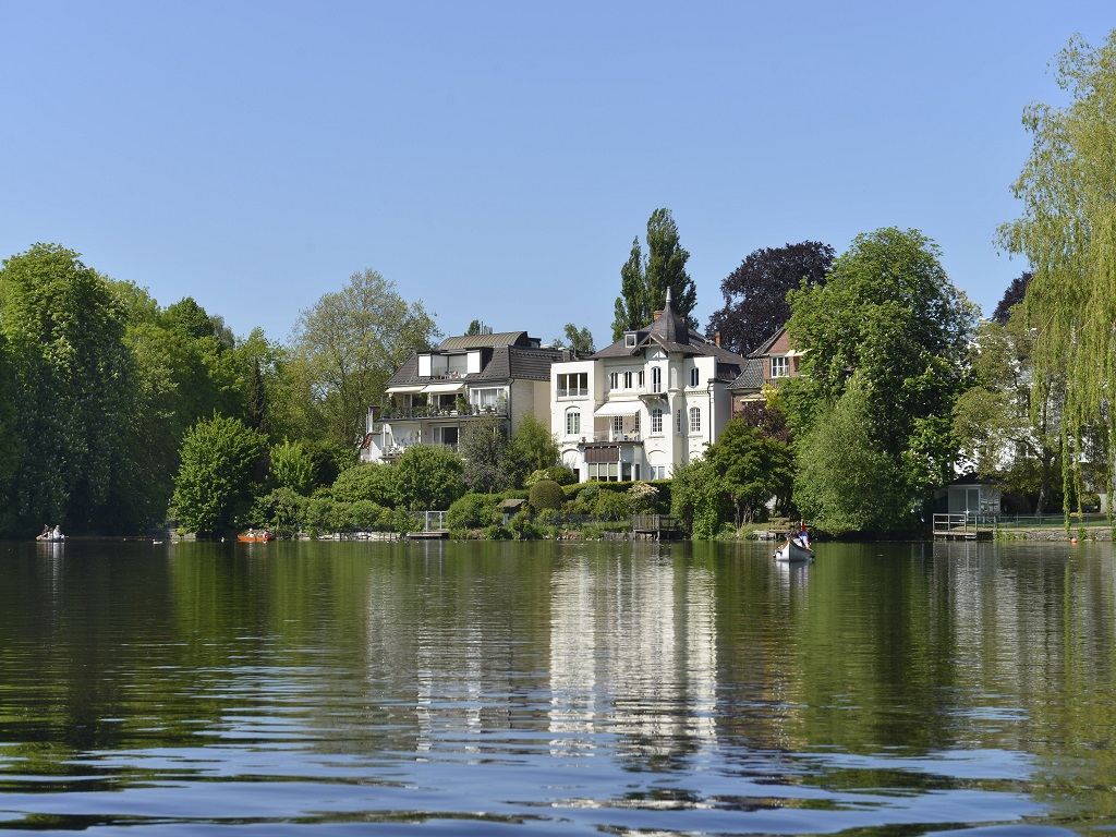 Ein Paddelboot auf dem Wasser. Im Hintergrund eine weiße Villa direkt am Ufer.