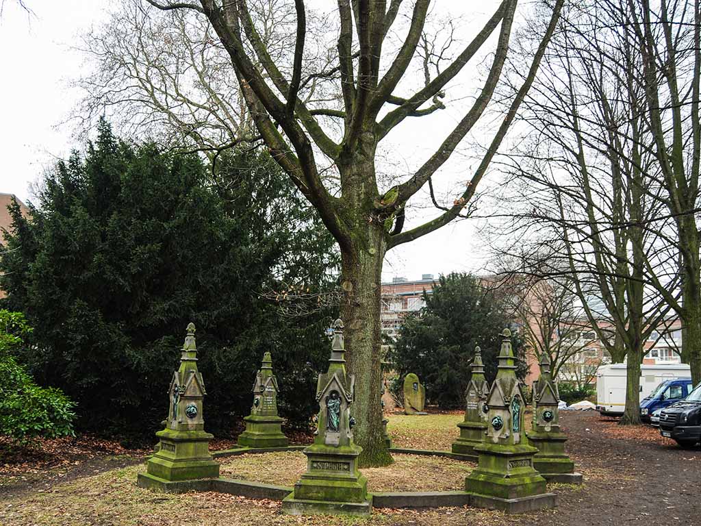 Gedenksteine mit Spitze stehen um einen Baum herum.