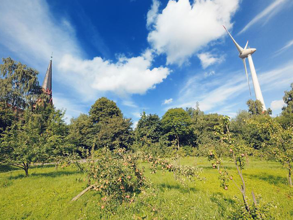 Die Kirchenwiese Altenwerder vor der St. Gertrud Kirche. Im Hintergrund ragt ein Windrad in den Himmel