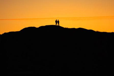 orangefarbener Himmel, in schwarz eine Hügellandschaft und oben drauf zwei Leute