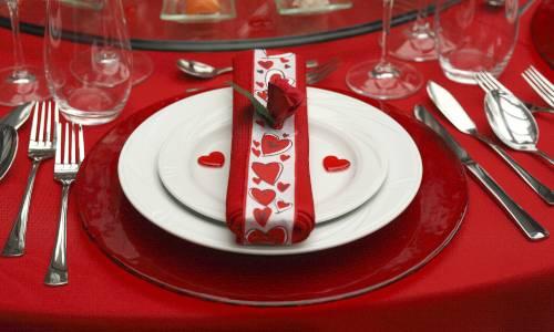 Rot gedeckter Tisch mit Teller auf dem eine Serviette mit Herzen liegt
