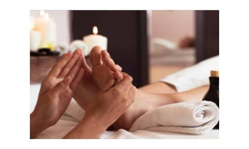 Zwei Hände massieren Füße einer Person die auf einer Liege mit Handtüchern liegt
