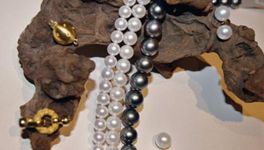 Eine weiße und eine schwarze Perlenkette liegen auf einem Holzstück