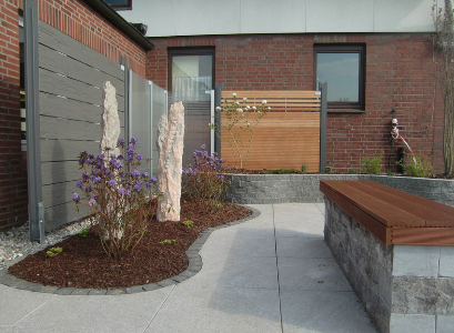 Gartenausstellung- eingerahmtes Beet, graue Fliesen, Bank aus Stein und Sitzfläche aus Holz sowie Sichtschutzwände aus Naturholz