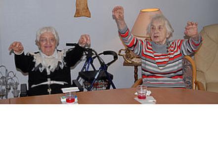 Zwei ältere Frauen sitzen an einem Tisch und heben die Arme in die Luft