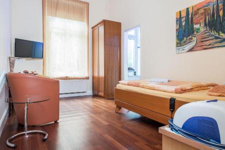 Innenansicht Patientenzimmer der Praxisklinik Brahmsallee, ein Kleiderschrank, ein Bett und ein Sessel auf einem Holzfußboden