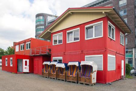Außenansicht, rote Containerhäuser mit Strandkörben davor
