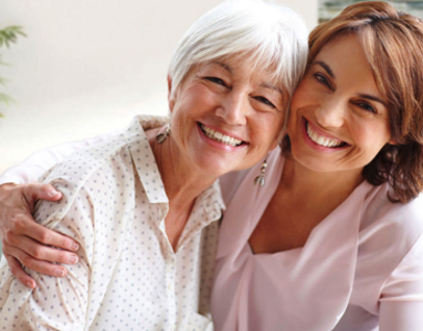 Eine Frau hat eine ältere Dame im Arm, beide lächeln