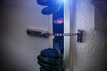 Ein Einbrecher macht eine Tür auf und wird durch Türschloss gehindert hereinzukommen