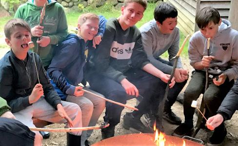 Sechs Jungs sitzen um ein Lagerfeuer und grillen Marshmellos
