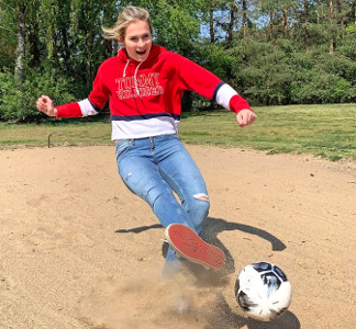 Ein Mädchen steht in einer Sandgrube und schießt den Fußball