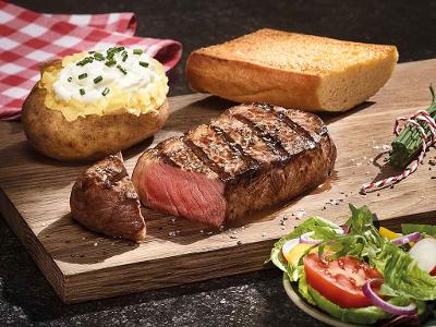 Ofenkartoffel mit SourCreme, ein Knoblauchbrot und ein Steak auf einem Holzbrett- davor steht ein Salalt
