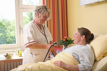 Krankenschwester misst Blutdruck bei im Bett liegender Patientin