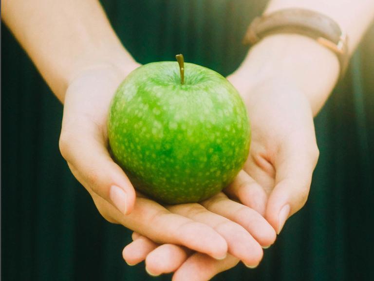 Zwei Hände halten einen grünen Apfel