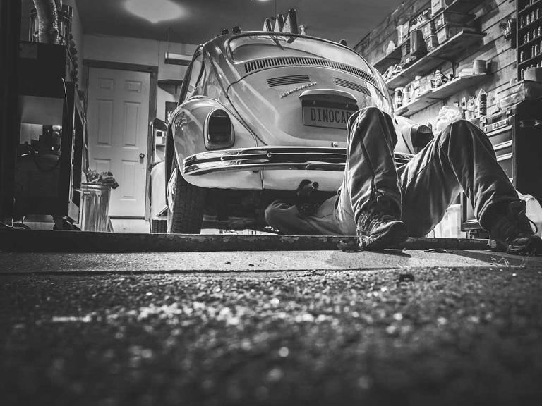 Ein Mann liegt in einer Werkstatt unter einem Auto, schwarz-weiß-Bild
