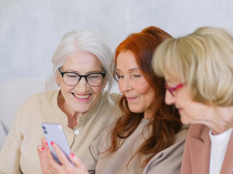 Drei ältere Damen schauen gemeinsam auf ein Handy