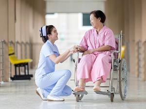 Eine Pflegerin hält die Hand einer Dame im Rollstuhl