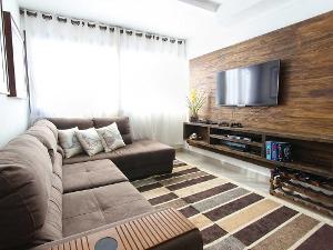 Ecksofa mit Holzwand an der ein Fernseher hängt, darunter ein Sideboard- alles in braunen Naturtönen gehalten