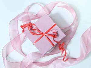 Ein Geschenk eingepackt in rosa Papier mit rotem Geschenkband und rosafarbenem Schleifenband drumherum liegend