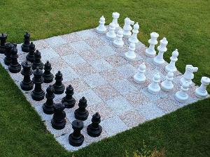 Schachbrett aus Fliesen auf einer Wiese mit schwarzen und weißen Schachfiguren