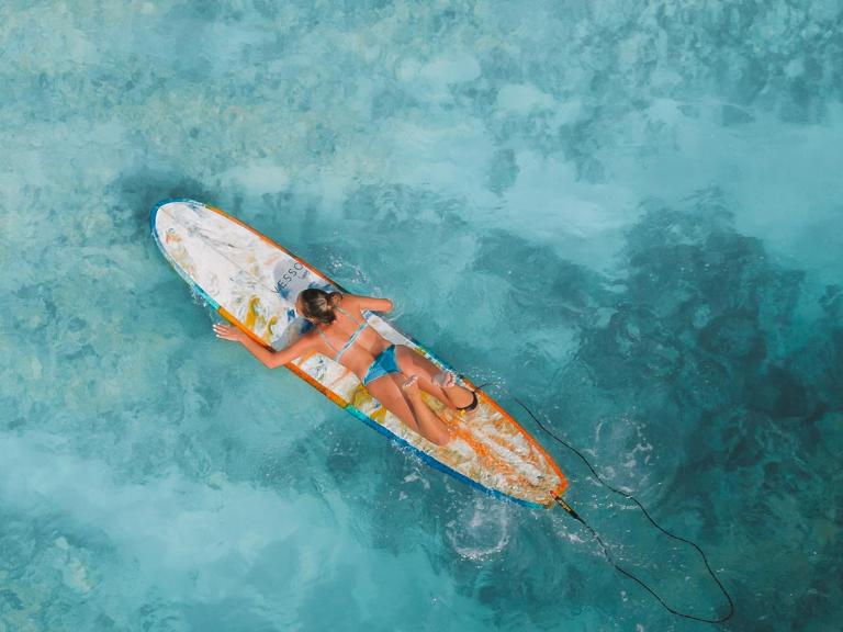 Frau liegt auf einem Surfbrett im Wasser, Aufnahme von oben