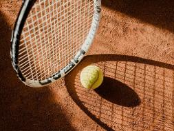 Tennisschläger und Tennisball auf einem roten Sandboden, Aufnahme von oben