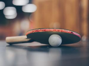 Tischtennisschläger liegt schräg auf einem Tischtennisball auf einer Tischtennisplatte