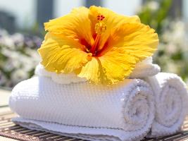 Aufgerollte weiße Handtücher mit einer gelben Blüte oben drauf liegend
