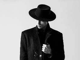 Mann mit Hut der die Augen verdeckt in einem Mantel mit Stehkragen, schwarz-weiss-Foto