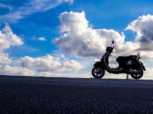 Motorroller steht an einer Straße, im Hintergrund der Himmel mit vereinzelten Wolken