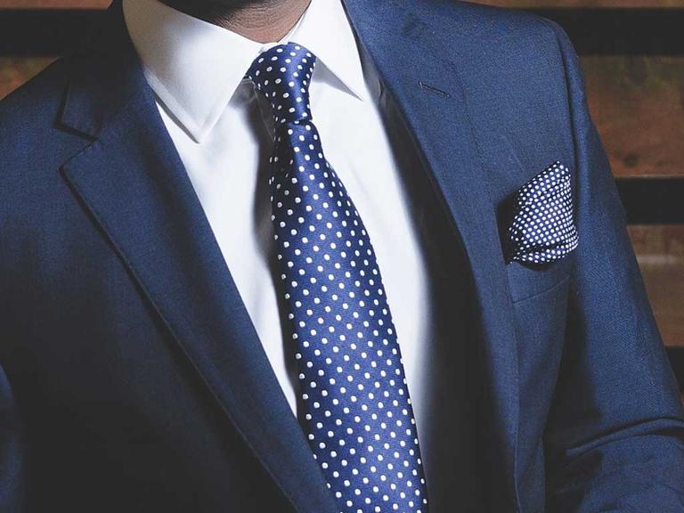 Ein Mann hat ein weißes Hemd an, einen marineblauen Anzug, eine blaue Krawatte und ein blaues Einstecktuch