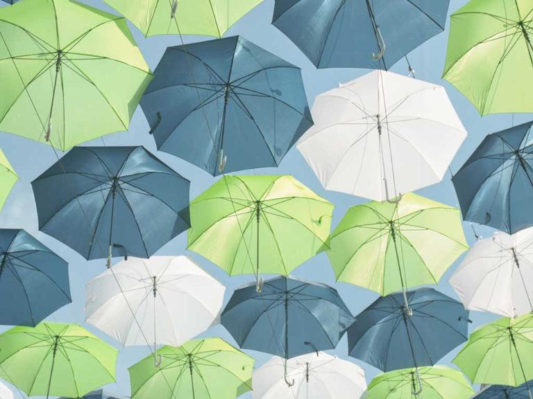 Aufgespannte Regenschirme in weiß, grün und blau steigen in den Himmel- Aufnahme nach oben in den Himmel