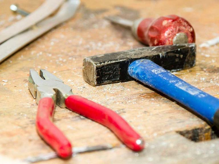Hammer, Schraubenzieher und Zange liegen auf einem Holztisch