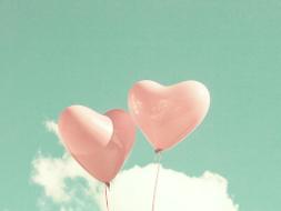 Zwei rosafarbene Herzluftballons schweben in den Himmel