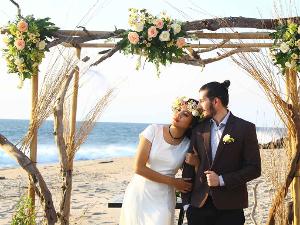 Ein Brautpaar steht unter einem geschmückten Holzrahmen am Strand