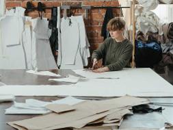 Eine Frau arbeitet an einem großen Tisch an Kleidungsvorlagen aus Papier und schneidet diese zurecht